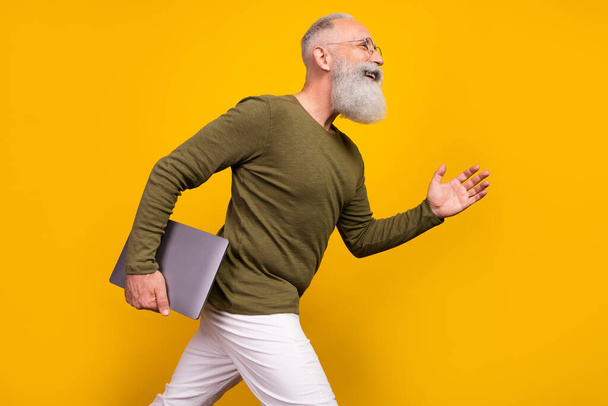 Profile photo of funny aged grey beard man hold laptop go wear eyewear green sweater isolated on yellow color background. - Fotó, kép