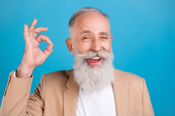 Portrait of handsome cheerful grey-haired man showing ok-sign winking advert isolated over bright blue color background. - Φωτογραφία, εικόνα