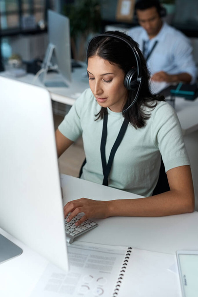 Foto de una mujer joven usando un auricular y un ordenador en una oficina moderna - Foto, Imagen