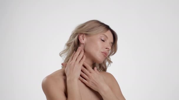 Esercizio di sollevamento della pelle. Donna di mezza età ben curata massaggiandosi il collo, applicando lozione idratante sul suo corpo, sfondo bianco dello studio, rallentatore - Filmati, video