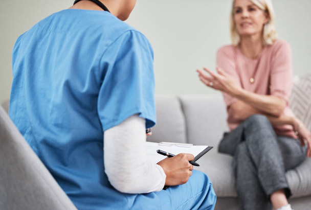 Fotografía de una enfermera sentada con un portapapeles durante una consulta con un paciente - Foto, imagen