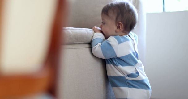 Bebé aprendiendo a ponerse de pie apoyándose en el sofá del hogar. Desarrollo infantil infantil - Foto, imagen