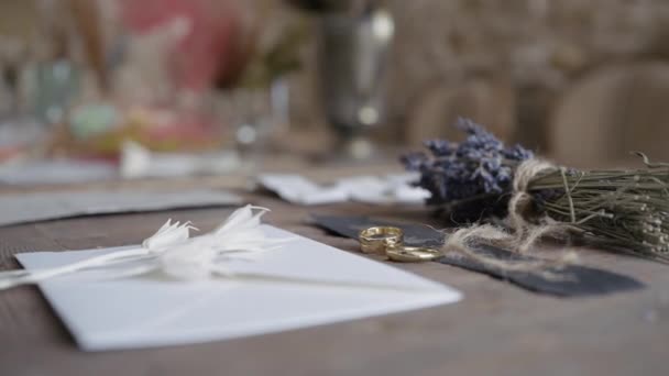 Detailní záběr na stůl se snubními prsteny. Akce. Stůl se starožitnými detaily a zlatými párovými prsteny. Dopis s perem a kyticí leží na stole se snubními prsteny.  - Záběry, video