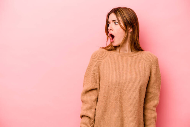 Young caucasian woman isolated on pink background being shocked because of something she has seen. - Photo, image