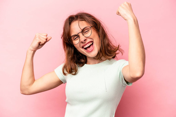 Young caucasian woman isolated on pink background cheering carefree and excited. Victory concept. - 写真・画像