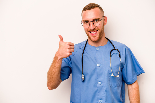 młody biały pielęgniarz człowiek izolowany na białym tle uśmiechając się i podnosząc kciuk w górę - Zdjęcie, obraz