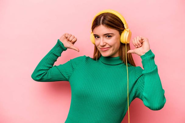 Jeune femme caucasienne écoutant de la musique isolée sur fond rose se sent fière et confiante, exemple à suivre. - Photo, image
