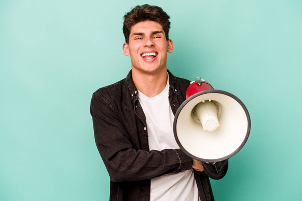 Jeune homme caucasien tenant un mégaphone isolé sur fond blanc riant et s'amusant. - Photo, image