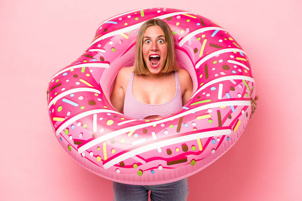 Young caucasian woman holding air mattress isolated on pink background - 写真・画像