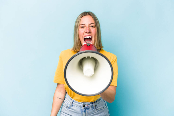Young caucasian woman holding a megaphone isolated on blue background - Fotografie, Obrázek