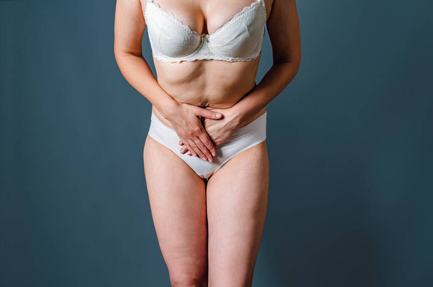 Kobieta w bieliźnie trzyma ręce zaciśnięte między nogami. Problemy ginekologiczne, nietrzymanie moczu, zdrowie i higiena kobiet, rozstępy na skórze - Zdjęcie, obraz