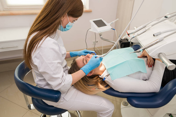 Dentist-hygienist conducts a teeth cleaning procedure for a girl in a dental clinic. Removal of tartar. The concept of dentistry, dental treatment. - Valokuva, kuva