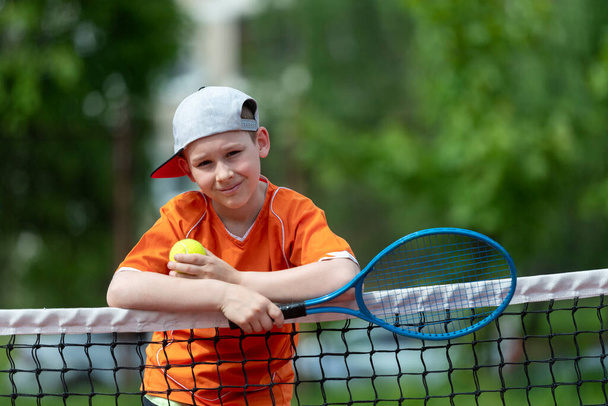 Gyermek teniszütővel a teniszpályán. Képzés fiatal gyerekeknek, egészséges gyerekek. Horizontális sport téma plakát, üdvözlőlapok, fejlécek, weboldal és alkalmazás - Fotó, kép