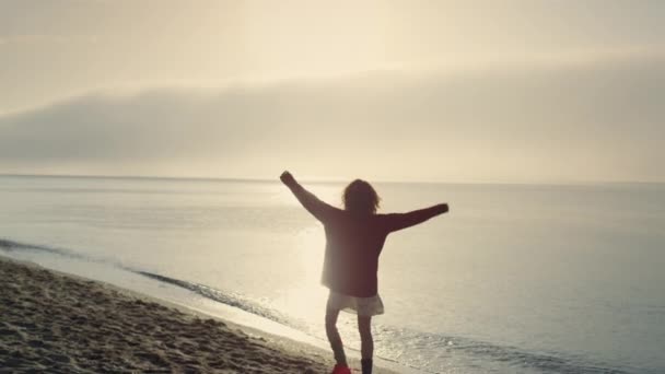 Gelukkig meisje op vakantie op het strand bij zonsopgang. Positieve vrouw die handen opsteekt. Vrouwelijke persoon viert overwinning. Emotionele vrouw die zich omdraait aan zee. Oceaan landschap in de ochtend. Vrijheid  - Video