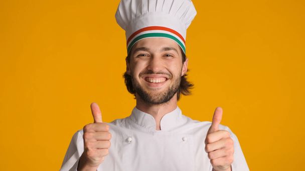 Üniformalı mutlu erkek aşçının portresi renkli bir arka planda kameraya başparmak kaldırıyor. Şef şapkası takmış yakışıklı bir adam onaylanmış bir jest yapıyor. - Fotoğraf, Görsel