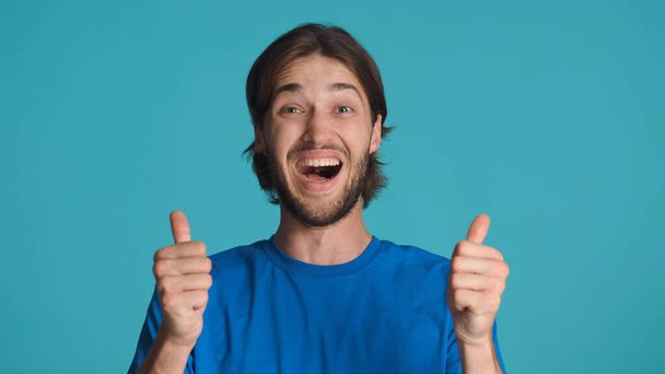 Overjoyed bearded man keeping thumbs up looking happy. Attractive guy sincerely smiling showing like gesture over colorful background - Photo, Image