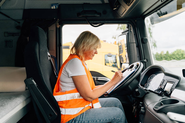 Mature woman truck driver steering wheel inside lorry cabin. Happy middle age female trucker portrait . High quality photo - Foto, afbeelding