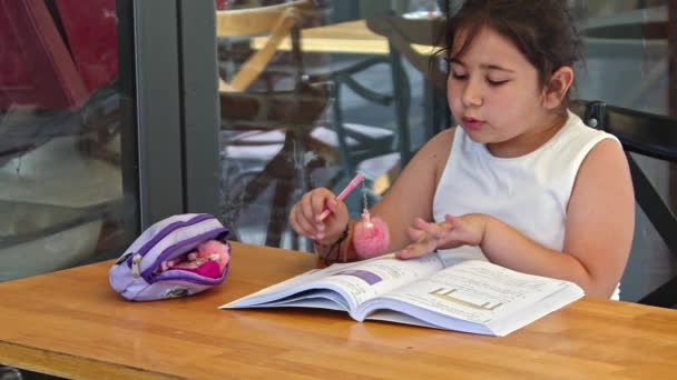 Pequeña niña trabajo escuela tarea al aire libre en durante la temporada de verano - Imágenes, Vídeo