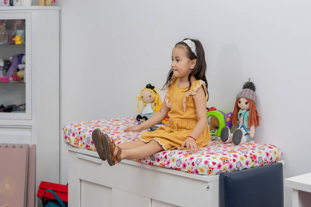 Latin girl sitting on a bed in a pediatric office waiting for the pediatrician. - Photo, Image
