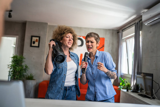 Zwei erwachsene erwachsene kaukasische Freundinnen oder Schwestern, die zu Hause Spaß haben Frauen, die tanzen und Karaoke singen, halten Mikrofon in der Hand und hören der Musik fröhliches Lächeln fröhlichen Rhythmus echte Menschen kopieren den Raum - Foto, Bild