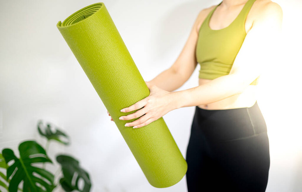 Vrouwelijke hand die groene yogamat vasthoudt om oefening op de mat voor te bereiden. - Foto, afbeelding