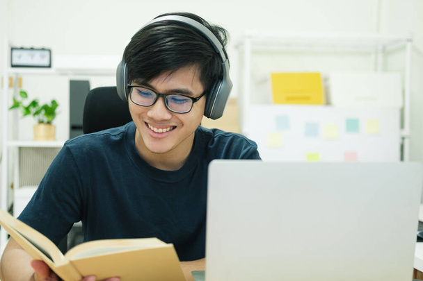 若い男性学生は家で勉強する。ノートパソコンを使ってオンラインで学ぶ.. - 写真・画像