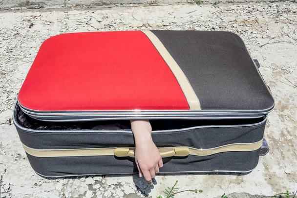 Mano femenina saliendo de una maleta. Imitación del asesinato de una mujer por un maníaco o asesino en serie. - Foto, imagen
