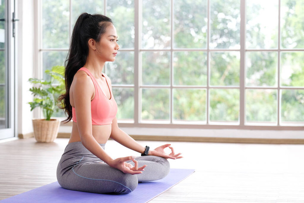 Asijky cvičit jóga meditace cvičení doma, Mladá asia žena sedí na podložce pro uvolněné jóga držení těla v dopoledních hodinách, cvičení doma, pohoda, duševní zdraví - Fotografie, Obrázek