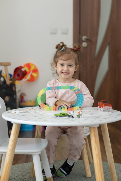 幸せな赤ん坊の女の子は家のテーブルの上でおもちゃで遊んでいる。ホーム活動。幼少期 - 写真・画像