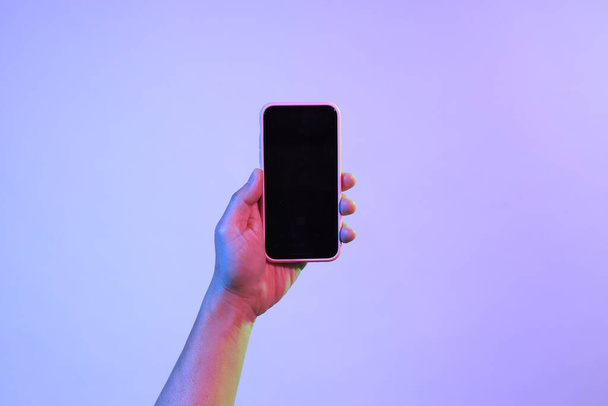Ο Ασιάτης κρατάει το έξυπνο τηλέφωνο κάτω από το έντονο χρώμα.. - Φωτογραφία, εικόνα