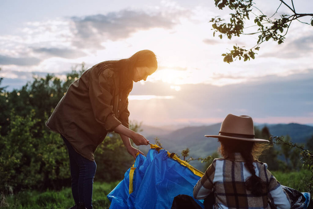 Selective focus of little daughter child in hat and young mother sets up tent near background summer mountains during sunset or sunrise, outdoor recreation. Travel, adventure, wanderlust concept - Foto, Imagen