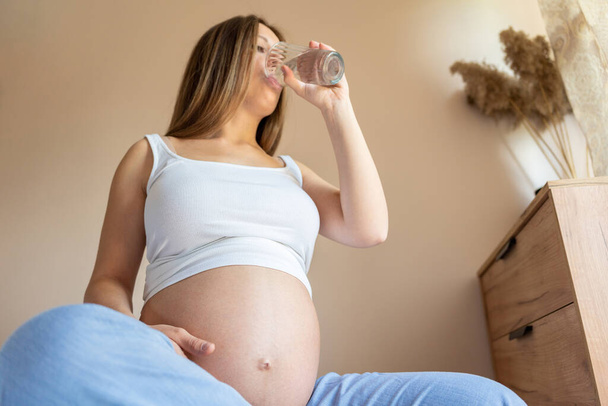 Trinkwasser schwangere Frau. Junge schwangere Mütter trinken Wasser. Schwangere wartet auf Baby. Glas Wasser. Konzept Mutterschaft, Geburt - Foto, Bild