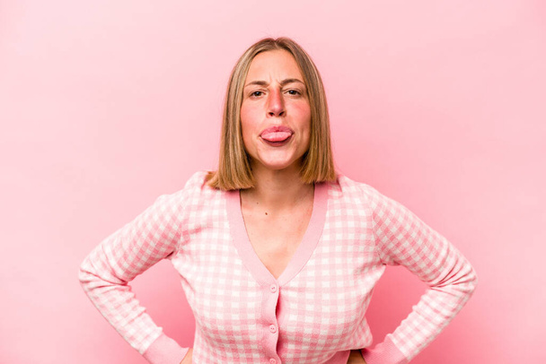 Joven mujer caucásica aislada sobre fondo rosa divertida y amigable sobresaliendo lengua. - Foto, Imagen