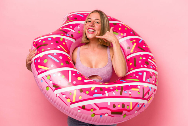 Young caucasian woman holding an air mattress isolated on pink background showing a mobile phone call gesture with fingers. - Foto, Imagem