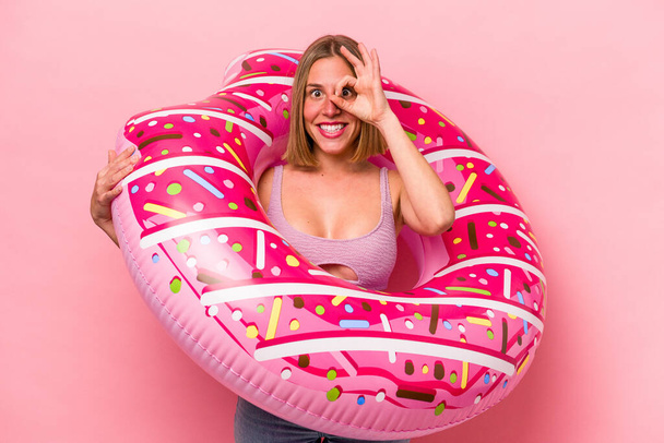 Young caucasian woman holding an air mattress isolated on pink background excited keeping ok gesture on eye. - Фото, зображення