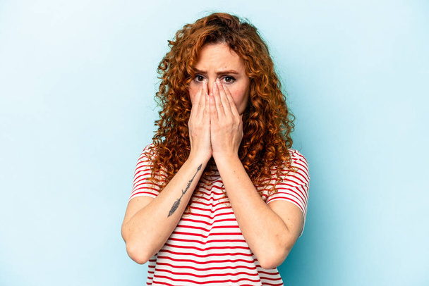 Young ginger caucasian woman isolated on blue background shocked covering mouth with hands. - Photo, Image