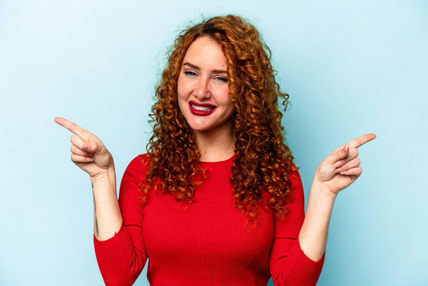 Young ginger caucasian woman isolated on blue background pointing to different copy spaces, choosing one of them, showing with finger. - Fotó, kép