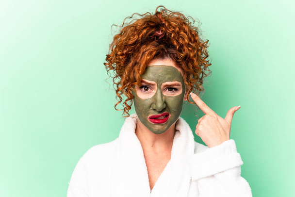 Young red hair woman with a facial aloe vera mask after a bath isolated showing a disappointment gesture with forefinger. - Photo, Image