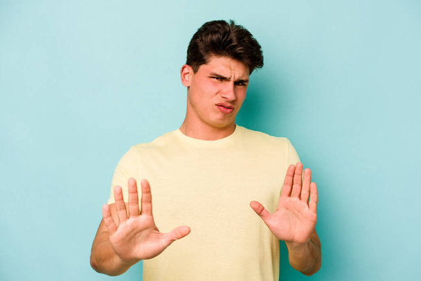 Молодий кавказький чоловік ізольований на синьому фоні, відкидаючи когось, хто показує жест огиди
. - Фото, зображення
