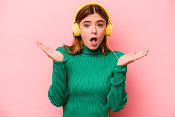 Молода біла жінка слухає музику ізольовано на рожевому фоні здивована і шокована
. - Фото, зображення
