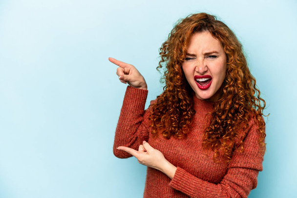Young ginger caucasian woman isolated on blue background pointing with forefingers to a copy space, expressing excitement and desire. - Foto, Bild