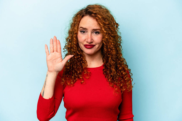 Молодая рыжая белая женщина, изолированная на синем фоне, весело улыбается, показывая номер пять пальцами.. - Фото, изображение