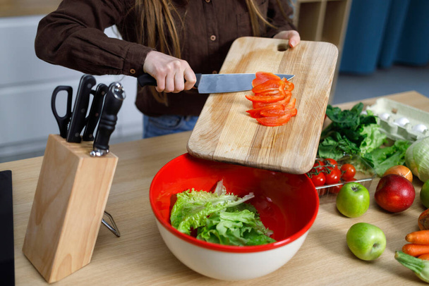 Dziewczyna w kuchni przygotowuje świeże sałatki krojenie warzyw rzucając czerwoną paprykę do miski - Zdjęcie, obraz
