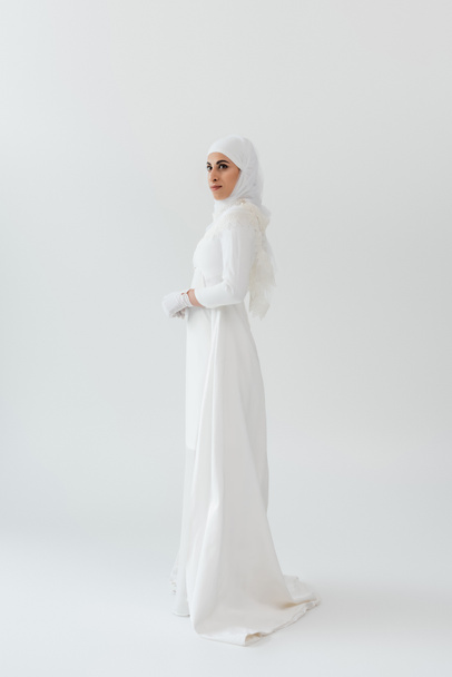 full length of young muslim bride in hijab and white dress on grey - Φωτογραφία, εικόνα