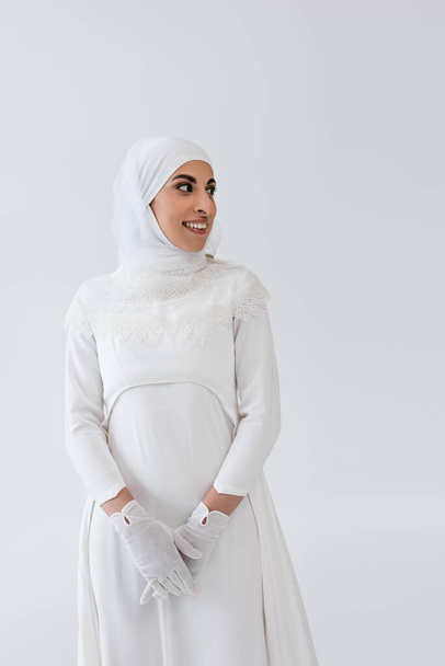 joyful muslim woman in hijab and wedding dress isolated on grey  - Photo, Image