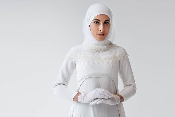 pretty muslim bride in gloves and wedding dress isolated on grey - Foto, Imagen