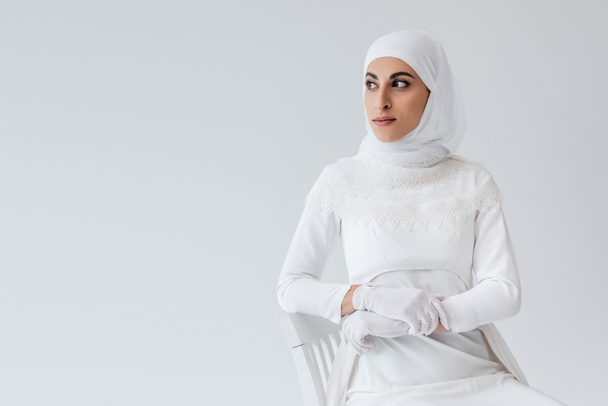 pretty muslim bride in gloves and wedding dress looking away isolated on grey - 写真・画像
