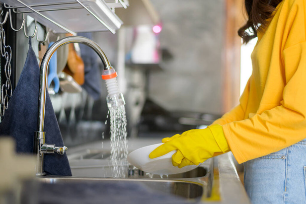 A Young happy woman wearing yellow gloves washing dishes in kitchen at home - Foto, imagen
