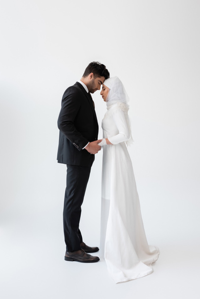 side view of muslim married couple holding hands and standing on grey - Photo, Image