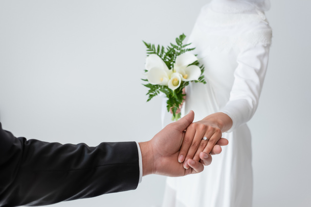 cropped view of bride with bouquet holding hands with blurred groom isolated on grey  - Photo, Image